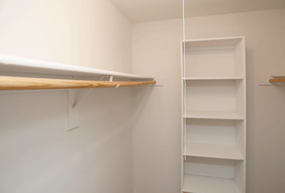 a walk in closet in a bedroom with white walls and a white shelf with a surfboard