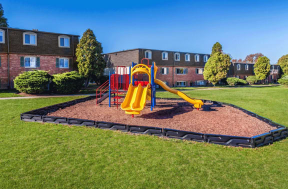 a playground with a yellow slide and red monkey bars in front of a brick building
