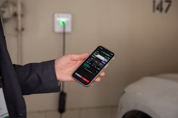 A person holding a smartphone with a charging station in the background.