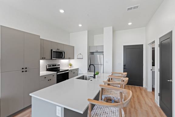 A modern kitchen with a white countertop and wooden chairs.