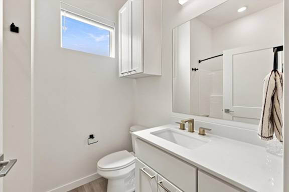 A white bathroom with a toilet, sink, and mirror.