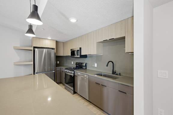 Modern kitchen with stainless steel appliances and a wooden accent wall at Brickside Heights, Millcreek, 84106