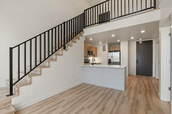 A modern kitchen with a black railing staircase.