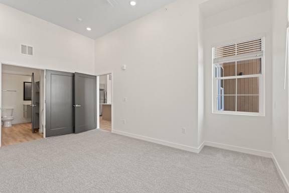 A large empty room with a grey carpet and a window with blinds.