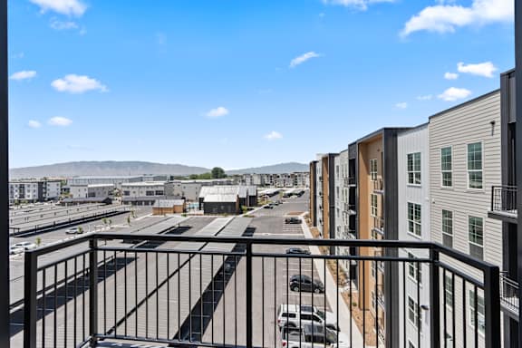 A view from a balcony overlooking a parking lot and a row of buildings.