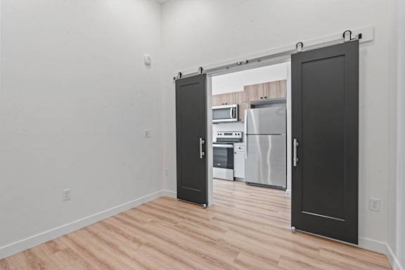 A kitchen with a black door is open to a room with a microwave, oven, and refrigerator.