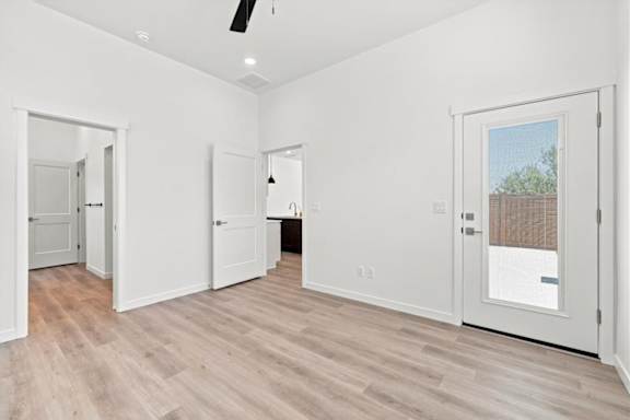 A room with white walls and wooden flooring, with a ceiling fan and a door leading outside.