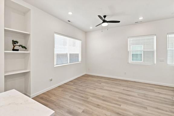 A room with a ceiling fan and two windows with blinds.
