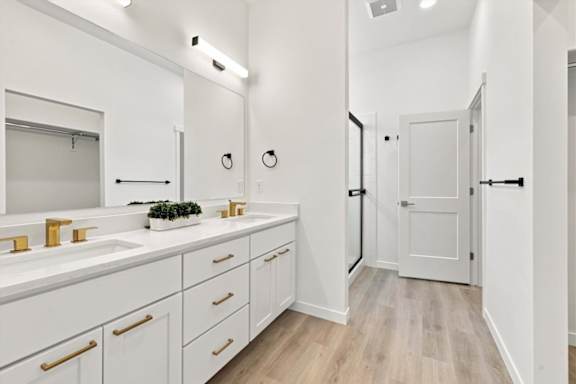 A white bathroom with a sink, mirror, and wooden floors.