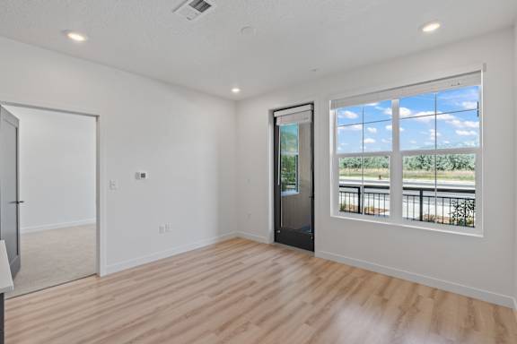 A room with a wooden floor and a window overlooking a balcony.