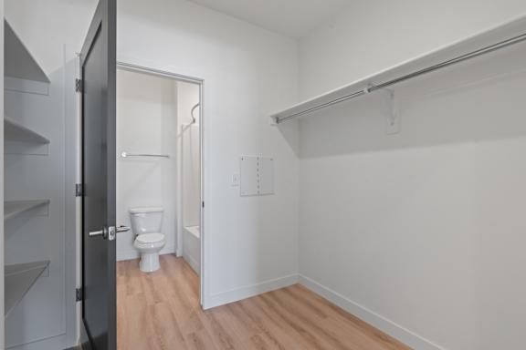 A white bathroom with a toilet and a doorway leading to another room.