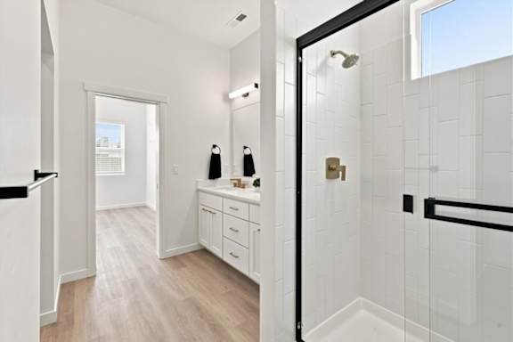 A bathroom with a white tile shower and a white vanity with a mirror.