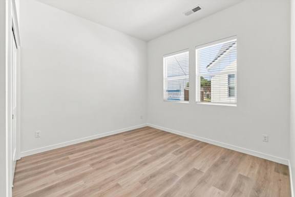 A room with wooden flooring and two windows.