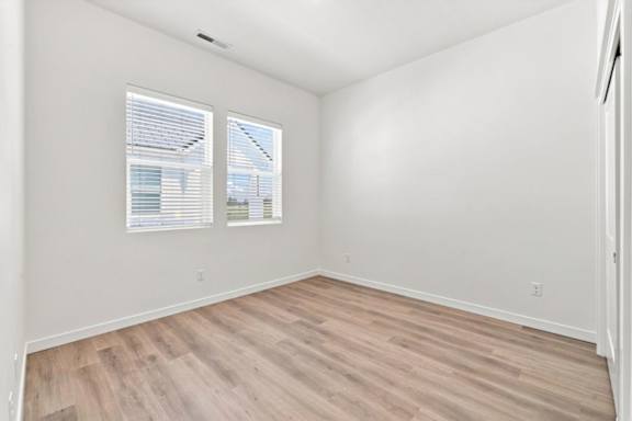A room with wooden flooring and two windows.