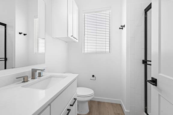 A white bathroom with a toilet, sink, and a window.at Alante Homes at Spring Run, Idaho