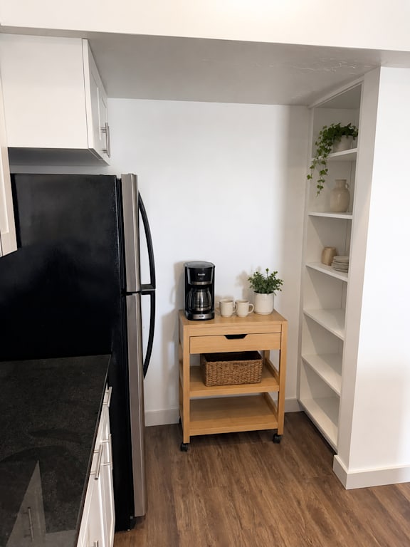 A black fridge sits next to a wooden table with a basket on it.