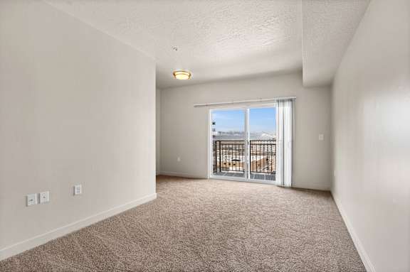 A room with a carpeted floor and a sliding glass door leading to a balcony. at Wilmington Flats Apartments, Salt Lake City, 84106