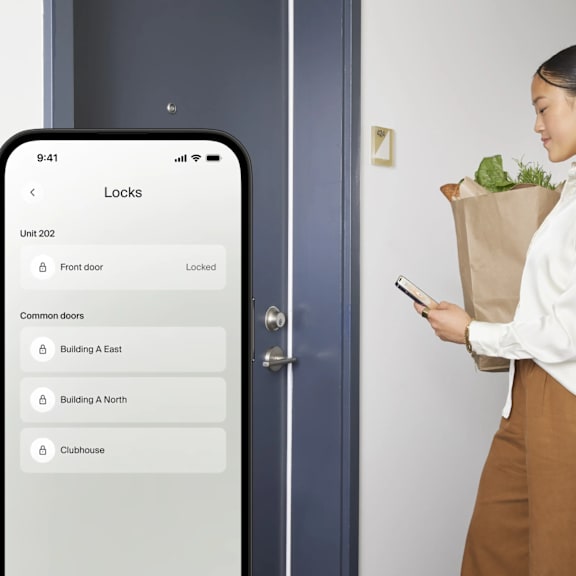 A woman is looking at her phone while standing in front of a door.