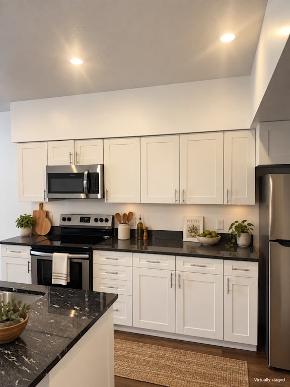 A kitchen with white cabinets and black countertops.