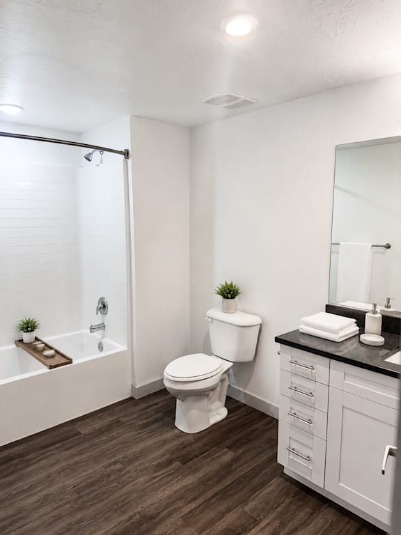 A white toilet sits in a bathroom with a wooden floor and white walls.