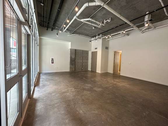 A large empty room with a concrete floor and walls, and a ceiling with exposed pipes and ducts at Paperbox Lofts Apartments, Apartments, Salt Lake City  , UT