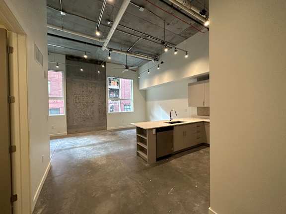 A large, empty room with a kitchenette and a window overlooking a cityscape at Paperbox Lofts Apartments, Apartments, Salt Lake City  , UT