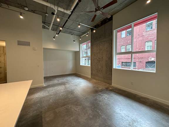 A large empty room with a white table and a window overlooking a red building at Paperbox Lofts Apartments, Salt Lake City  , UT, 84101