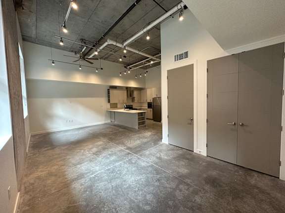 A large, empty room with concrete floors and walls, and a ceiling with exposed pipes and lights at Paperbox Lofts Apartments, Salt Lake City