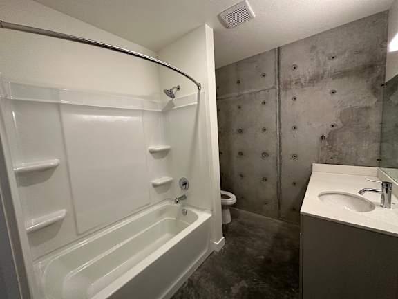A white bathtub with a shower head and a white sink with a silver faucet. at Paperbox Lofts Apartments, Salt Lake City  , UT, 84101