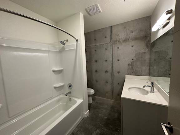 A white bathtub with a shower head and a white sink with a silver faucet at Paperbox Lofts Apartments, Salt Lake City  , Utah