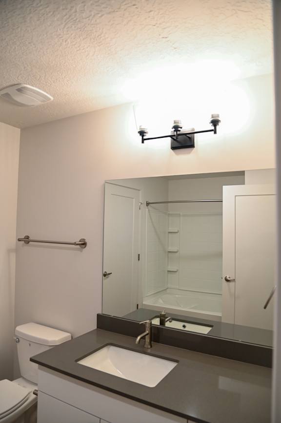 A bathroom with a toilet, sink, mirror, and shower.
