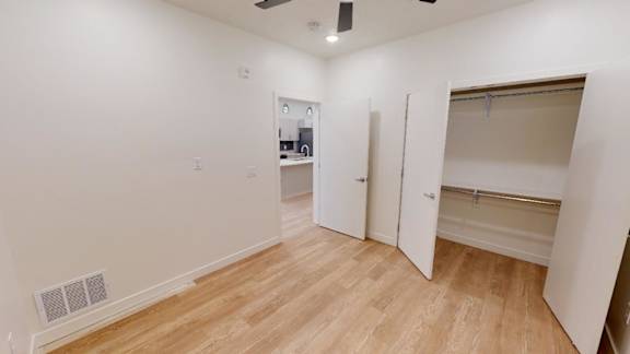 A room with wooden flooring and white walls, with a door open to another room.