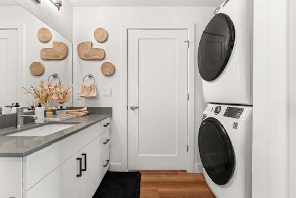 A white laundry room with a washing machine and a mirror.
