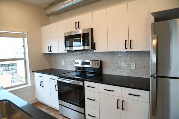 A kitchen with white cabinets and black countertops.