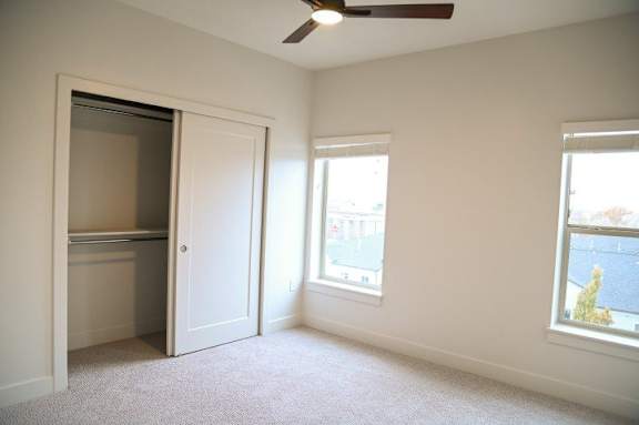 A room with a ceiling fan and two windows.