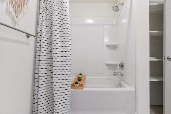A white bathroom with a shower curtain and a wooden tray with a plant on it. at Paperbox Lofts Apartments, Salt Lake City  , Utah