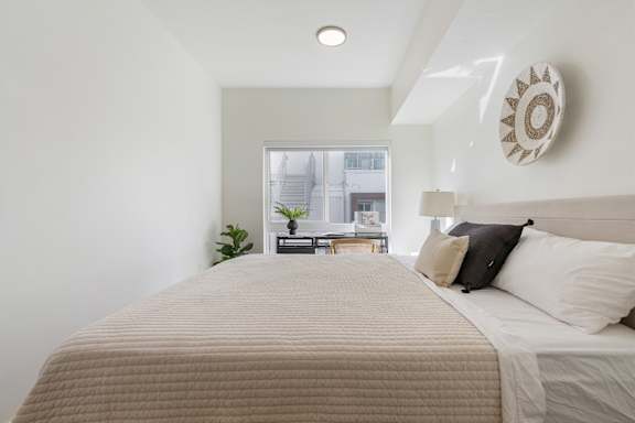 A bed with a beige comforter and two pillows in a room with a window. at Paperbox Lofts Apartments, Salt Lake City