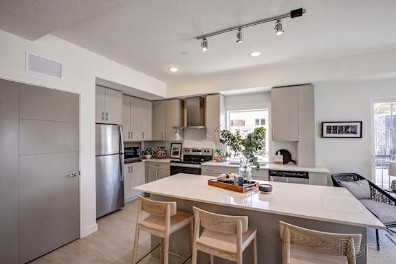 A modern kitchen with a white island and wooden chairs. at Paperbox Lofts Apartments, Salt Lake City  , Utah