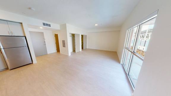 A spacious room with a refrigerator on the left and a large window on the right. at Paperbox Lofts Apartments, Salt Lake City  , 84101