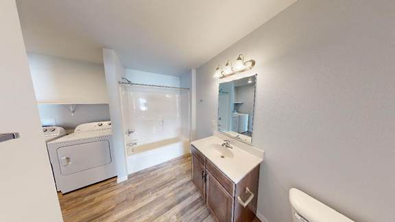 A white bathroom with a wooden vanity and a white toilet at Red Rock Apartments, Rapid City