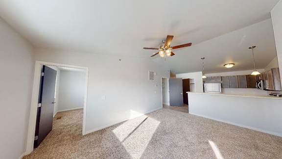 A spacious living room with a ceiling fan and carpeted floor at Red Rock Apartments, Rapid City, SD