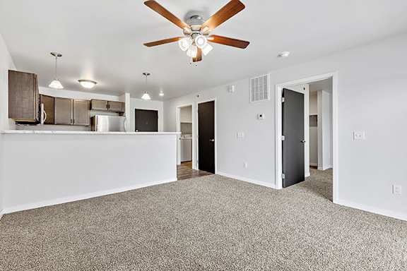 a living room with a ceiling fan and a kitchen in the background at Red Rock Apartments, Rapid City, SD