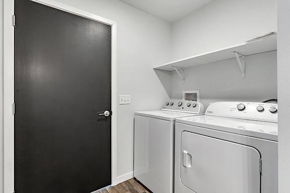 a laundry room with a white washer and dryer and a black door at Red Rock Apartments, Rapid City, South Dakota