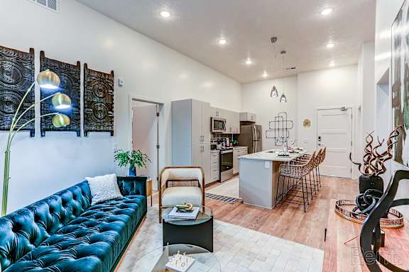 A blue tufted couch sits in a living room with a kitchen in the background.