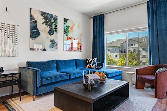 A living room with a blue couch and a painting on the wall.