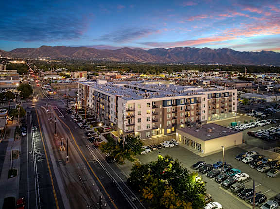 A city street with cars and apartment buildings with mountains in the background.