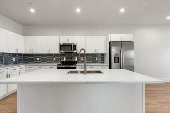 A modern kitchen with a white island and stainless steel appliances. at The Vue At Desert Color, St. George, Utah
