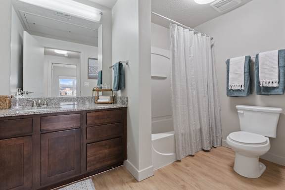 A white toilet sits next to a shower curtain in a bathroom. at Wilmington Flats Apartments, Apartments, Salt Lake City, UT