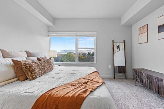 A bedroom with a large bed and a view of the mountains through the window. at Wilmington Flats Apartments, Salt Lake City