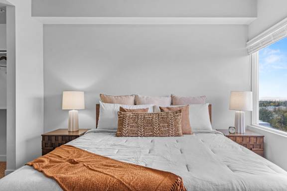 A bed with a white comforter and a brown throw blanket is in the center of the image. at Wilmington Flats Apartments, Utah, 84106